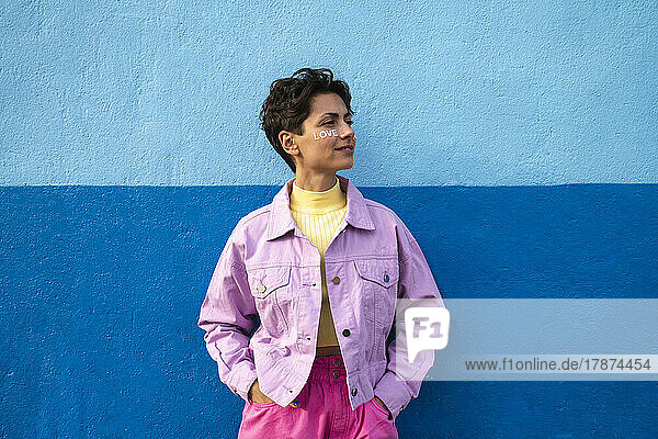 Woman with hands in pockets leaning on blue wall