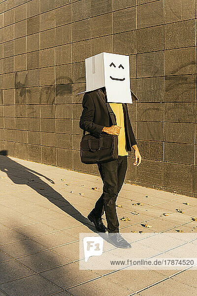 Businessman wearing box with smiley face walking on footpath