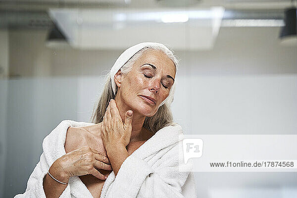 Frau mit geschlossenen Augen massiert den Hals im Badezimmer