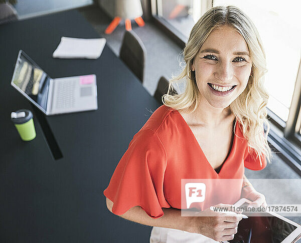 Happy blond businesswoman holding tablet PC in office