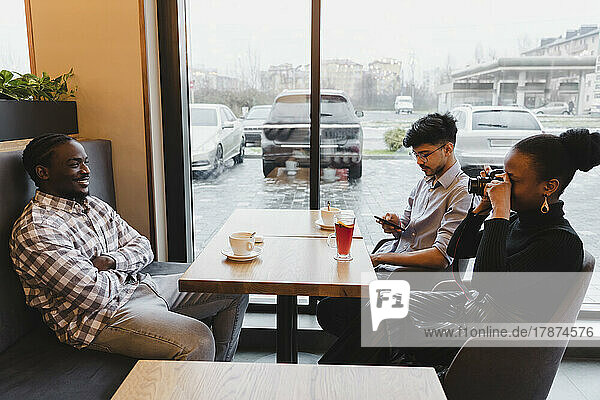 Junge Frau fotografiert Freund mit der Kamera im Café