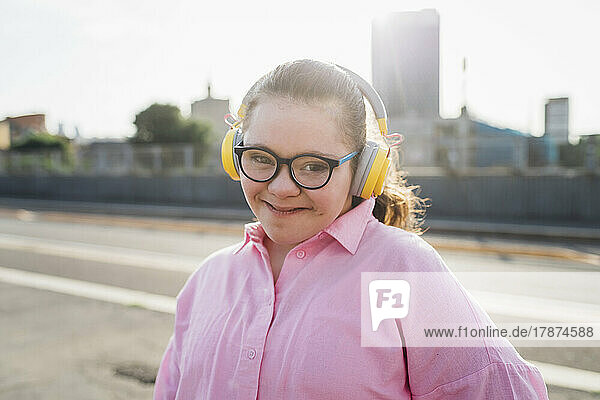 Smiling teenage girl with down syndrome listening music through headphones on sunny day