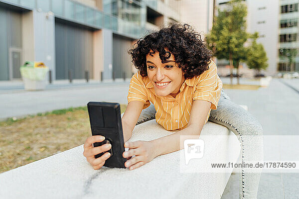 Smiling woman using smart phone sitting on bench