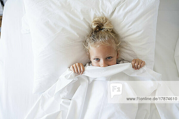 Girl peeking from blanket in bed