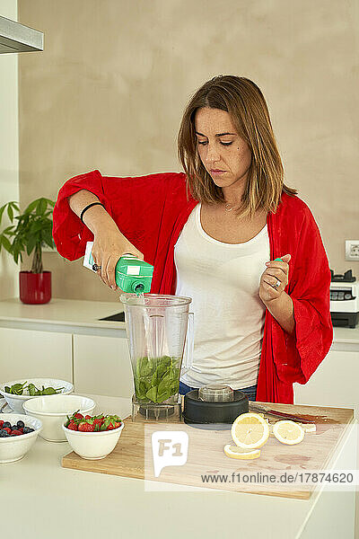 Woman preparing smoothie standing in kitchen at home