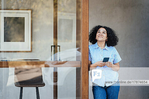 Lächelnde Frau mit Smartphone steht vor der Tür