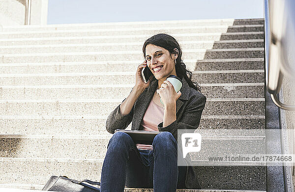 Happy transgender businesswoman talking on mobile phone sitting on steps