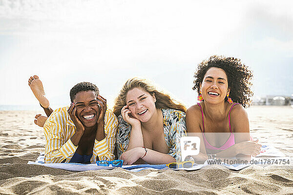 Happy multiracial friends lying on towel at beach