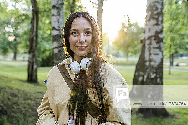Smiling woman with headphones standing in park