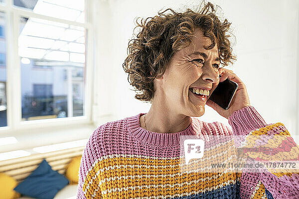 Cheerful woman talking on mobile phone at home