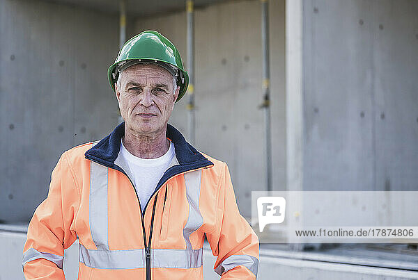 Confident construction worker wearing reflective clothing and hardhat standing at construction site