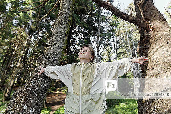 Smiling girl with arms outstretched standing amidst tree trunks