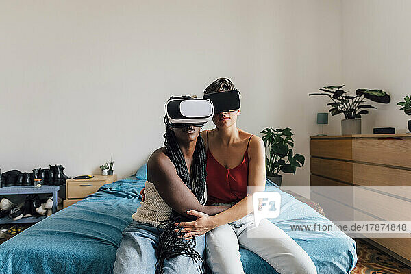 Lesbian couple wearing VR glasses sitting on bed at home