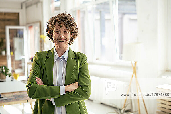 Happy businesswoman wearing green blazer standing with arms crossed in office