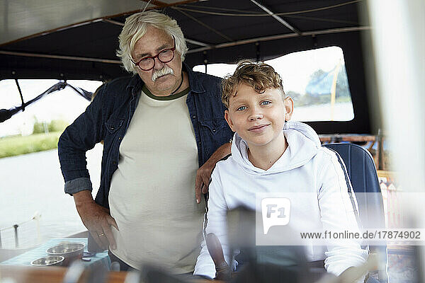 Senior man wearing eyeglasses standing by grandson in boat
