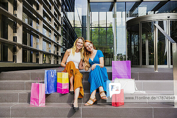 Happy friends with shopping bags on steps outside mall