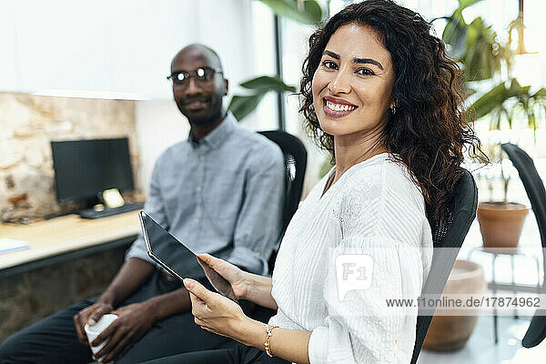 Lächelnde Geschäftsfrau mit Tablet-PC sitzt neben einem Geschäftsmann im Büro