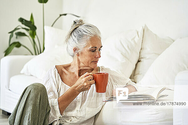 Mature woman with mug reading book in living room