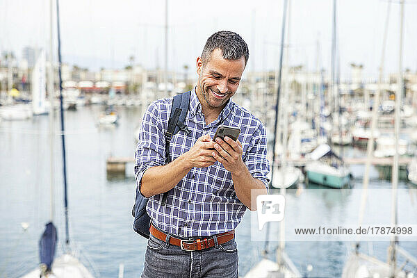 Happy mature man using mobile phone at harbor