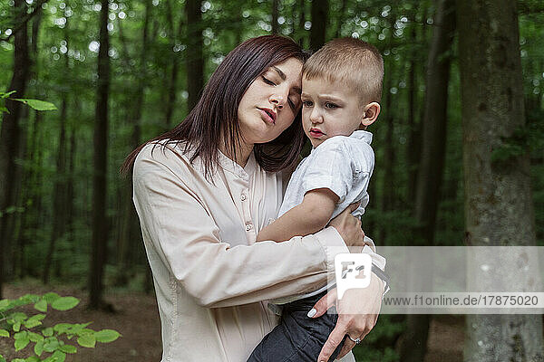 Mother with eyes closed carrying son in forest