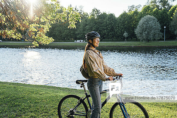 Lächelnde Frau mit Fahrrad steht am See im Park