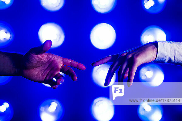 Hands of couple reaching towards each other in front of illuminated lights
