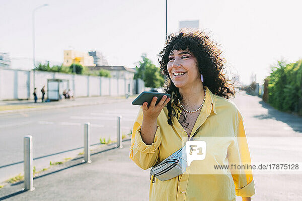 Smiling woman sending voicemail through smart phone on street
