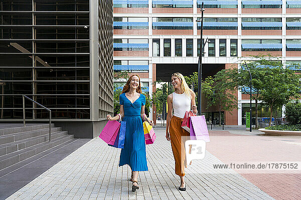 Fröhliche Freunde mit Einkaufstüten  die auf dem Fußweg spazieren gehen