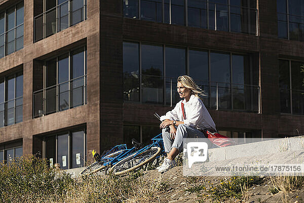 Smiling young woman sitting by bicycle on sunny day