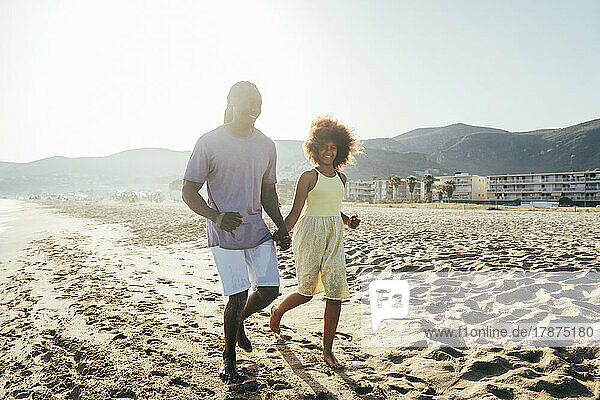 Father and daughter running at beach on sunny day