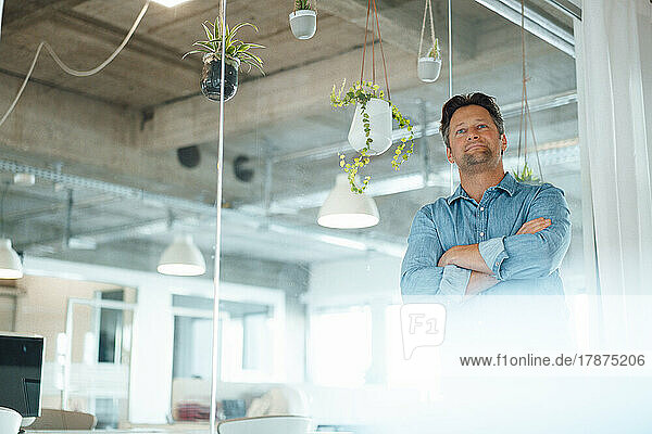 Contemplative mature businessman standing with arms crossed in office