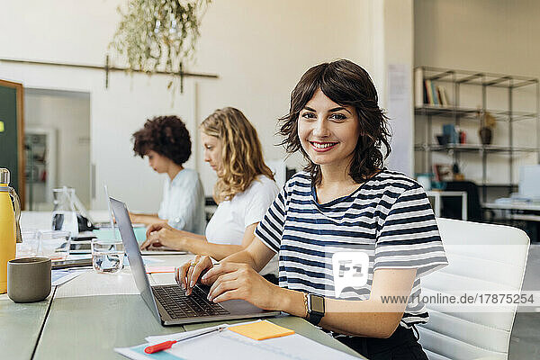 Smiling businesswoman with laptop at work place