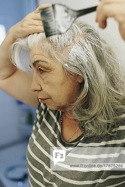 Senior woman applying dye with hairbrush at home