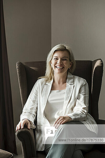 Happy mature woman sitting in armchair at home