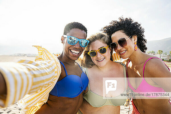 Multiracial friends wearing sunglasses taking selfie at beach