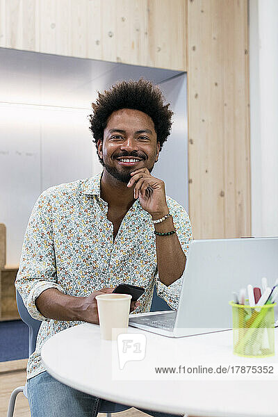 Portrait of smiling businessman with mobile phone and laptop in office