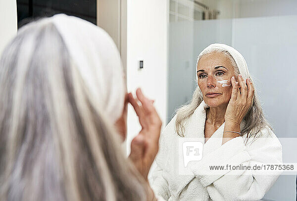 Reife Frau trägt Gesichtscreme im Badezimmer auf