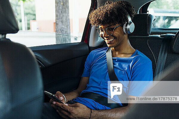 Smiling young man wearing wireless headphones texting through smart phone