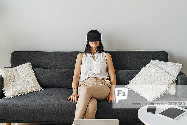 Frau mit Virtual-Reality-Brille sitzt zu Hause auf dem Sofa