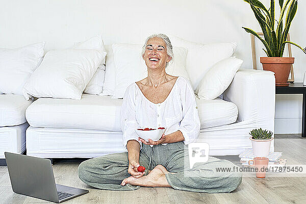 Woman laughing with bowl of strawberries in living room