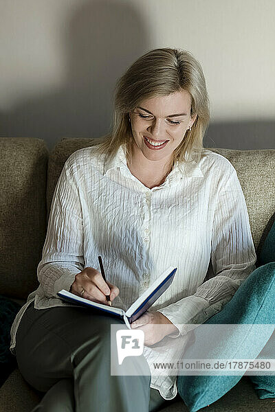 Happy mature woman writing in diary at home