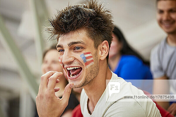 Excited man with American Flag painted on face shouting in stadium