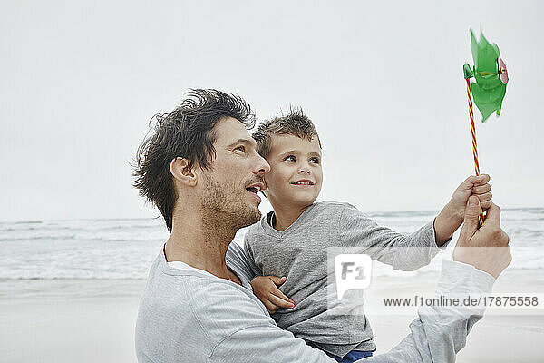 Father carrying son on the beach holding green pinwheel