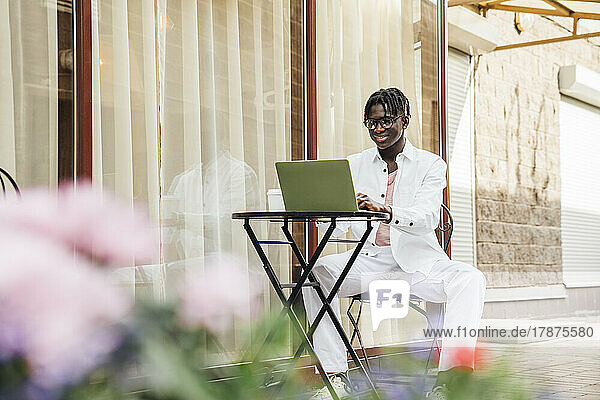 Smiling freelancer with laptop sitting at sidewalk cafe