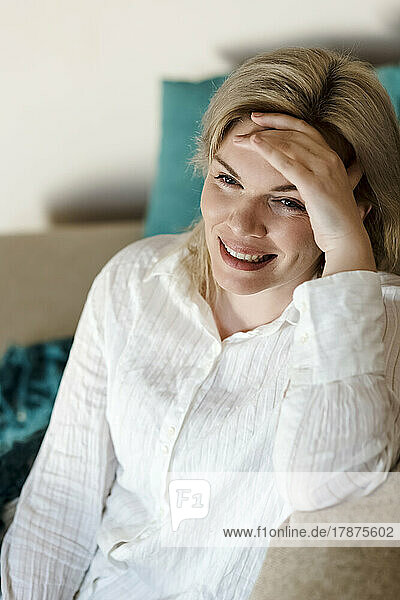 Smiling woman sitting with head in hand at home