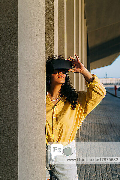 Woman wearing virtual reality simulator by column on footpath