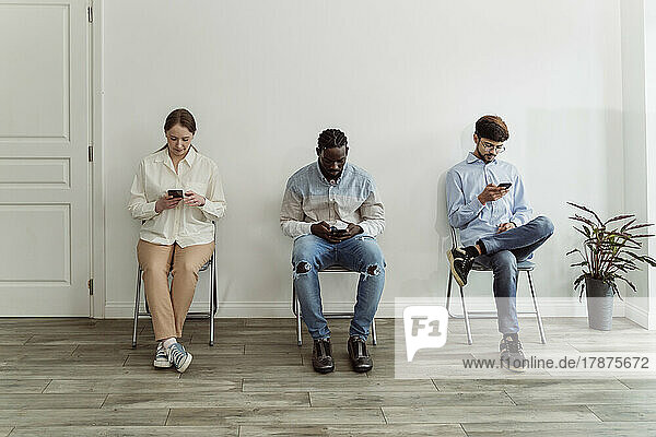 People using smart phones sitting on chairs in front of wall