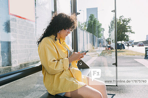 Young woman using smart phone sitting at bus stop