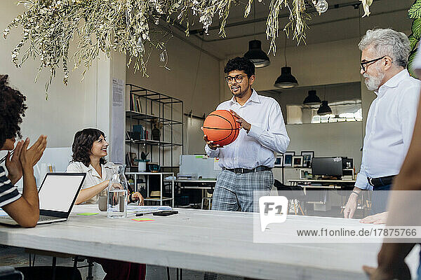 Businessman holding basketball talking with colleagues at office