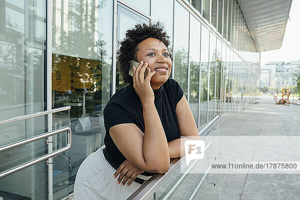 Smiling businesswoman talking on mobile phone leaning on railing